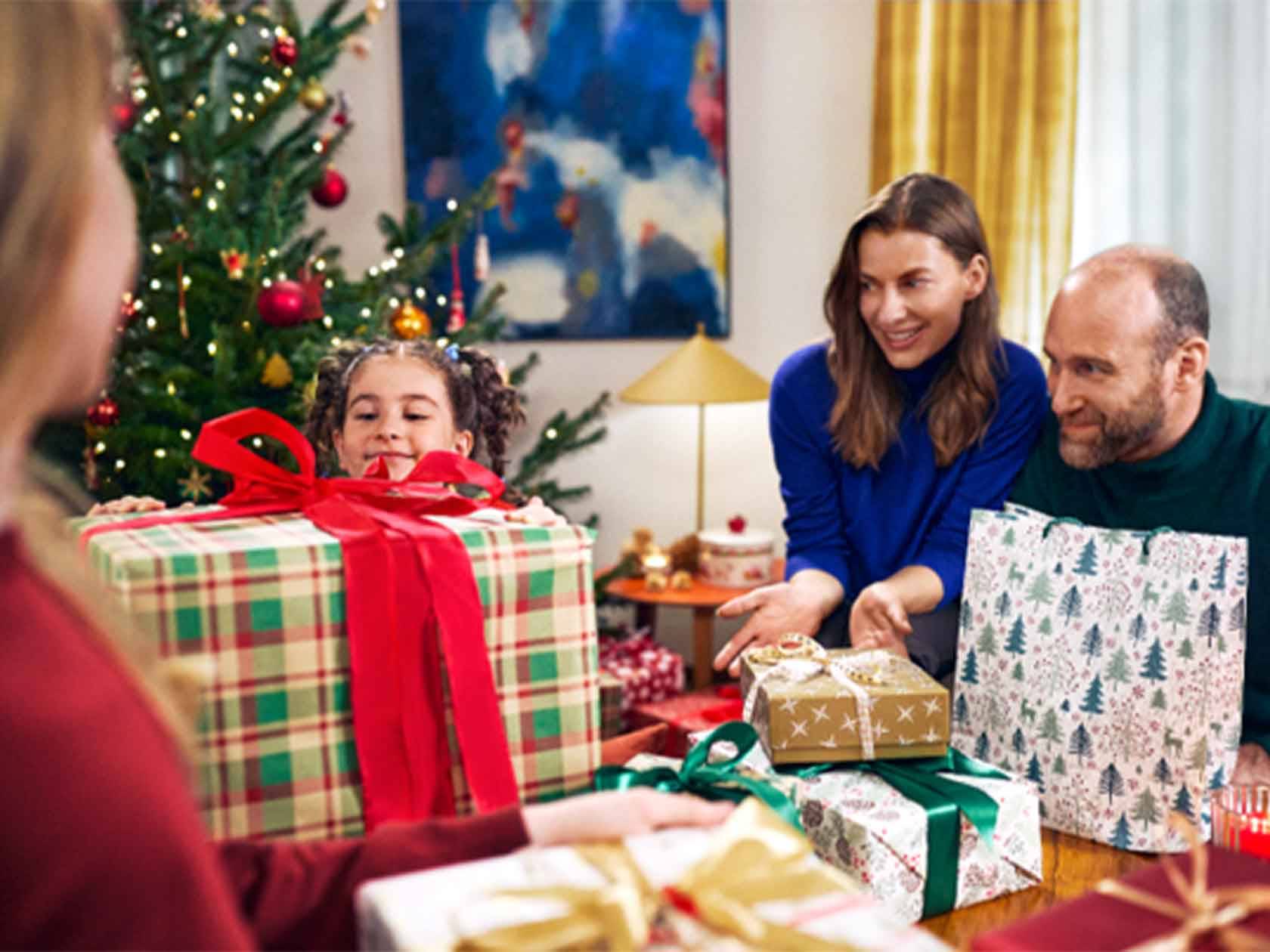 Család karácsonyi ajándékokat bont ki egy feldíszített karácsonyfa mellett.