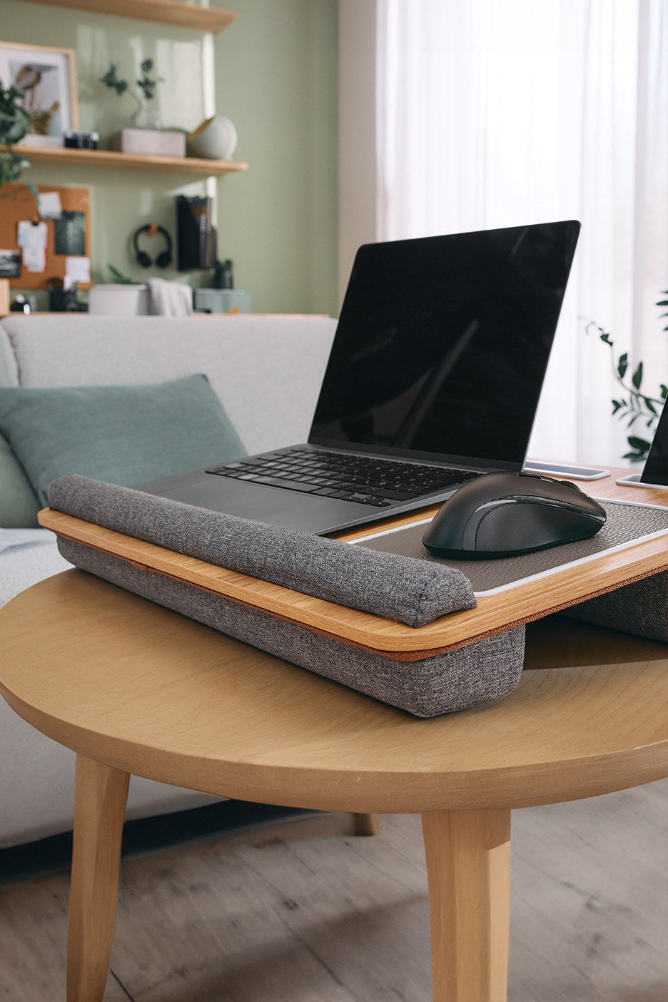 Laptop és egér egy fa asztalon, kanapé és polcok a háttérben.