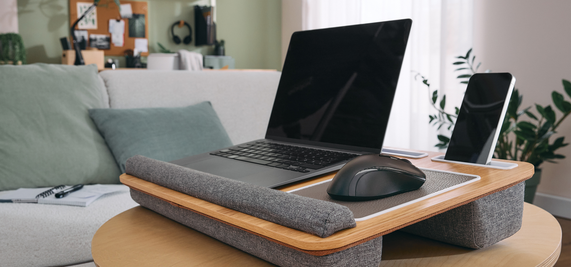 Laptop és egér egy fa laptoptartón, kanapé és konyha a háttérben.