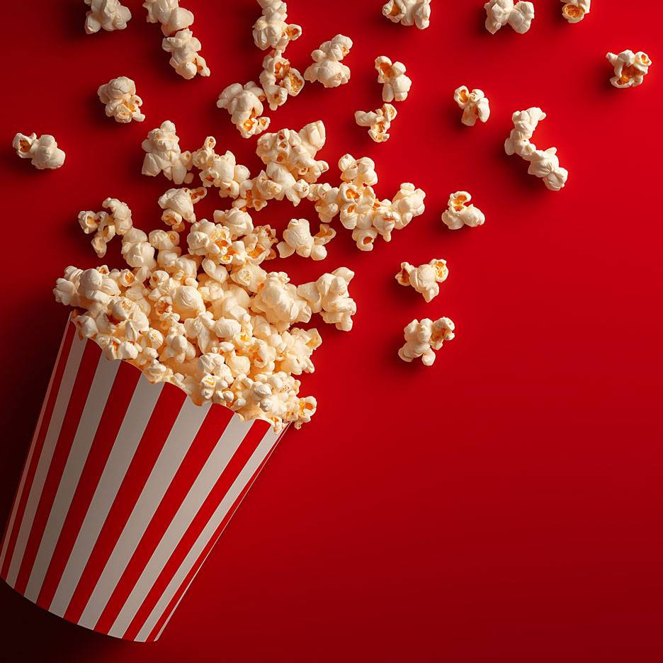 Popcorn piros háttéren, egy része csíkos kartonpohárban.