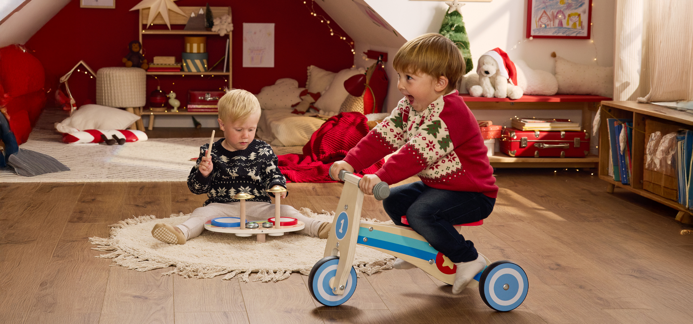 Két gyermek játszik karácsonyi pulóverben, karácsonyi dekorációval díszített szobában.