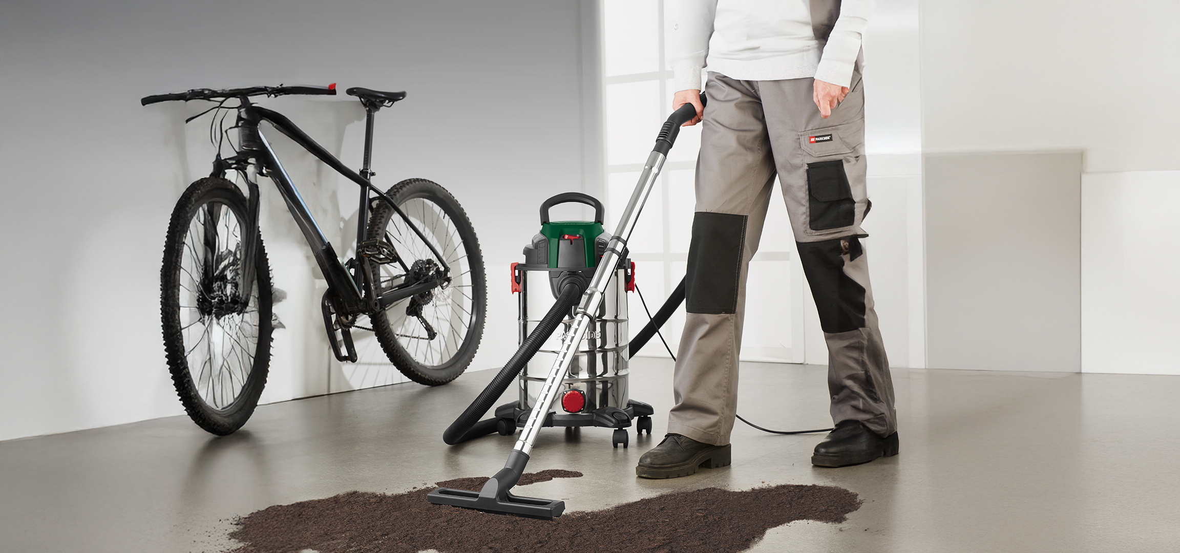Férfi porszívózik egy kerékpár mellett, nedves és száraz porszívóval.