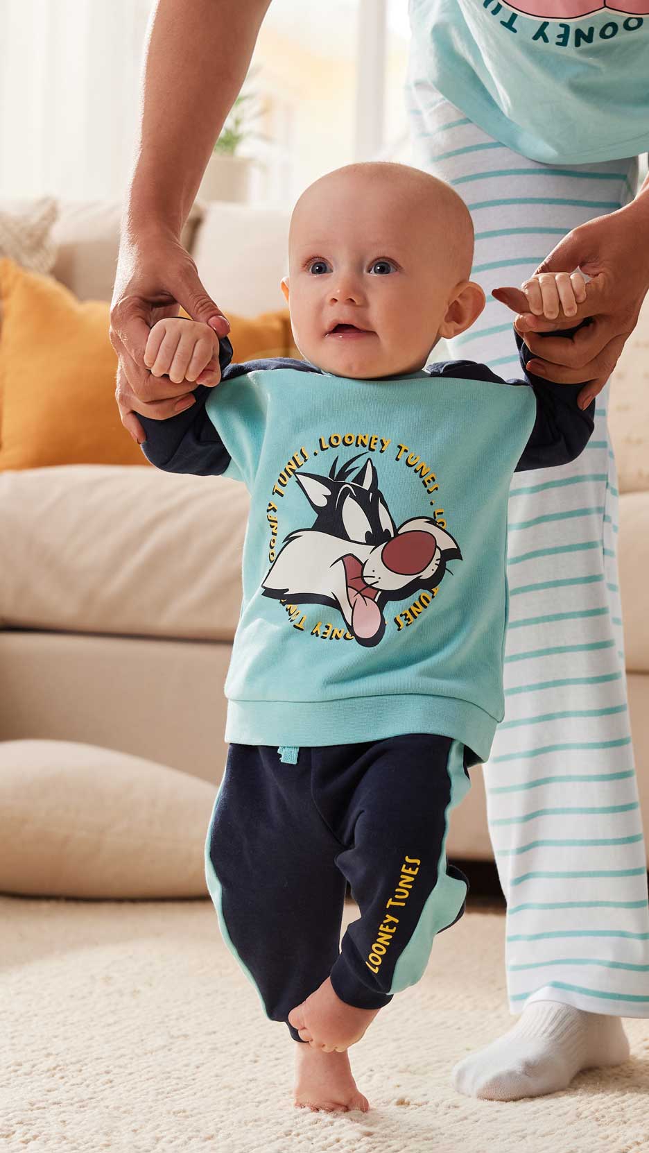 Egy baba Looney Tunes pizsamában, egy felnőtt kezét fogva.