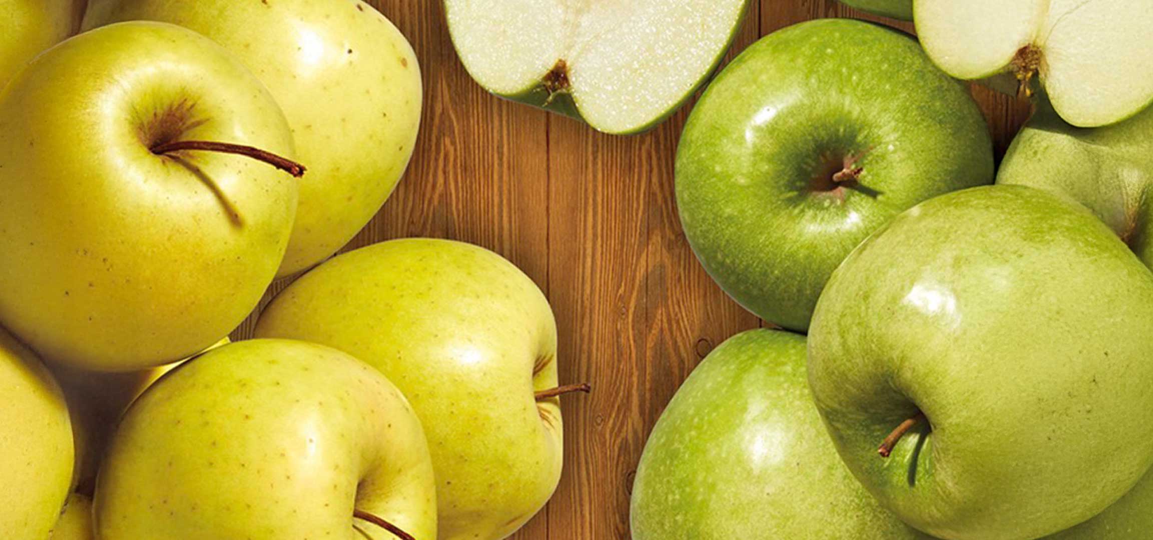 Sárga és zöld alma egy fa felületen, néhány félbevágva.